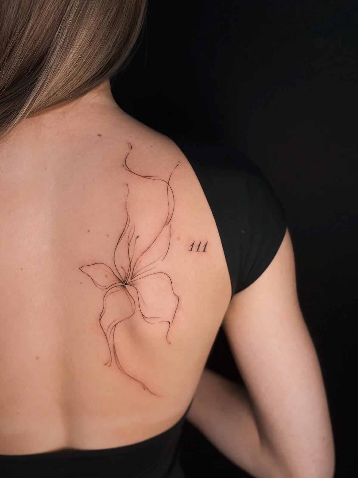 Filigranes Fineline-Tattoo einer abstrakten Blüte mit drei kleinen Strichen am oberen Rücken – Arbeit von Merci, Skin City Tattoo.