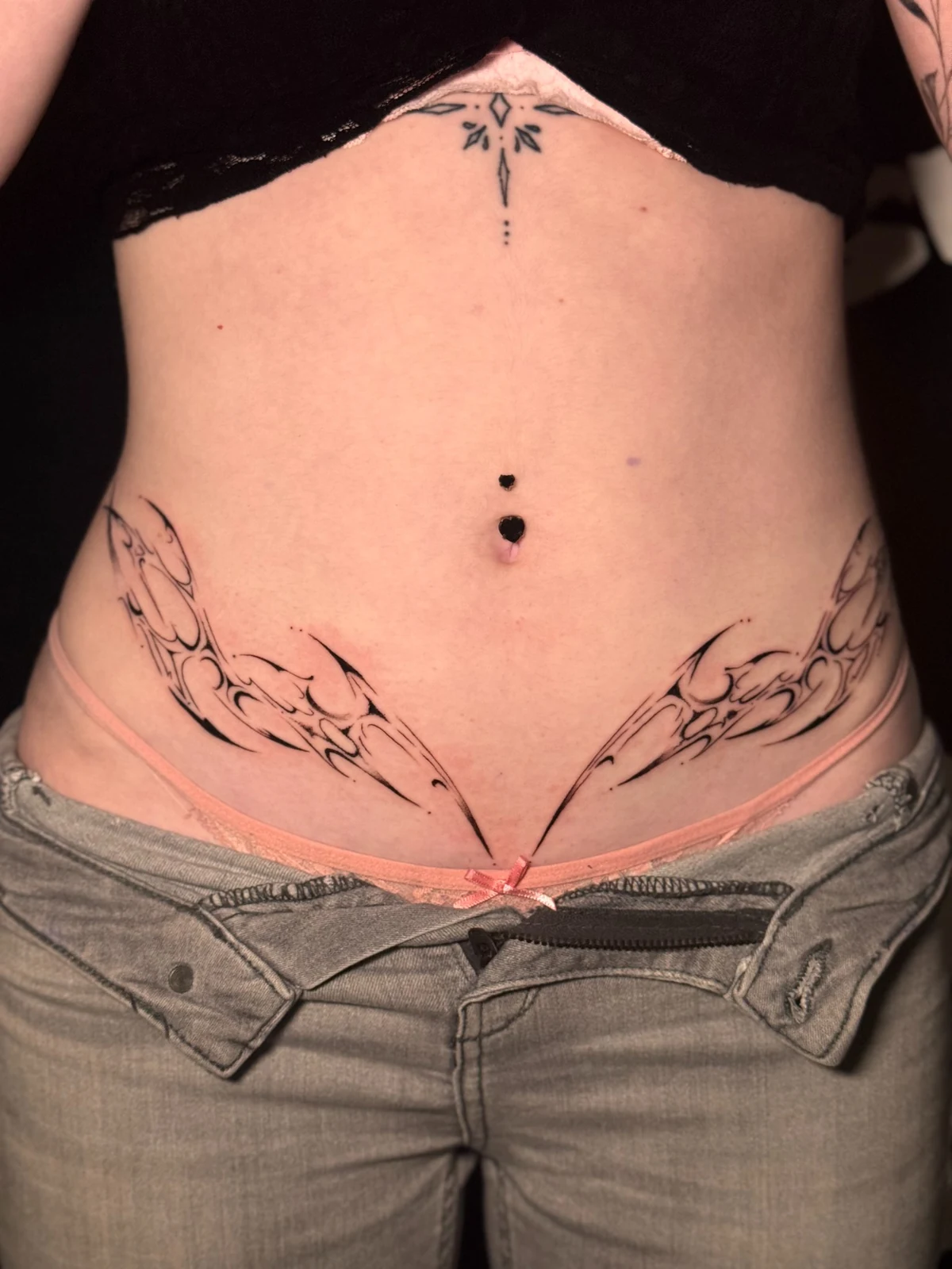 Symmetrisches Fineline-Tattoo mit abstrakten Ornamenten entlang des Unterbauchs – Arbeit von Merci, Skin City Tattoo.
