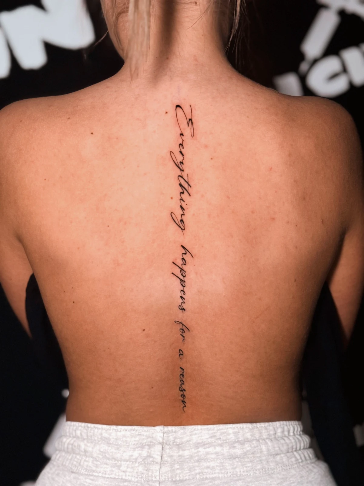 Feines vertikales Schriftzug-Tattoo entlang der Wirbelsäule – Arbeit von Merci, Skin City Tattoo.
