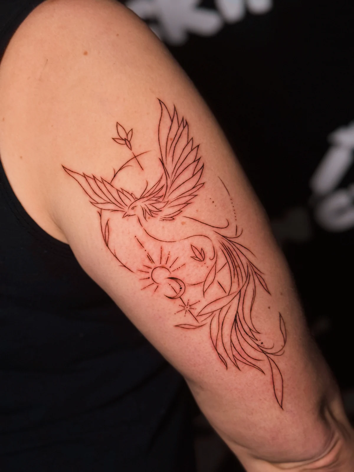 Fineline-Tattoo mit fliegendem Vogel, Sonne und floralen Linien am Oberarm – Arbeit von Merci, Skin City Tattoo.