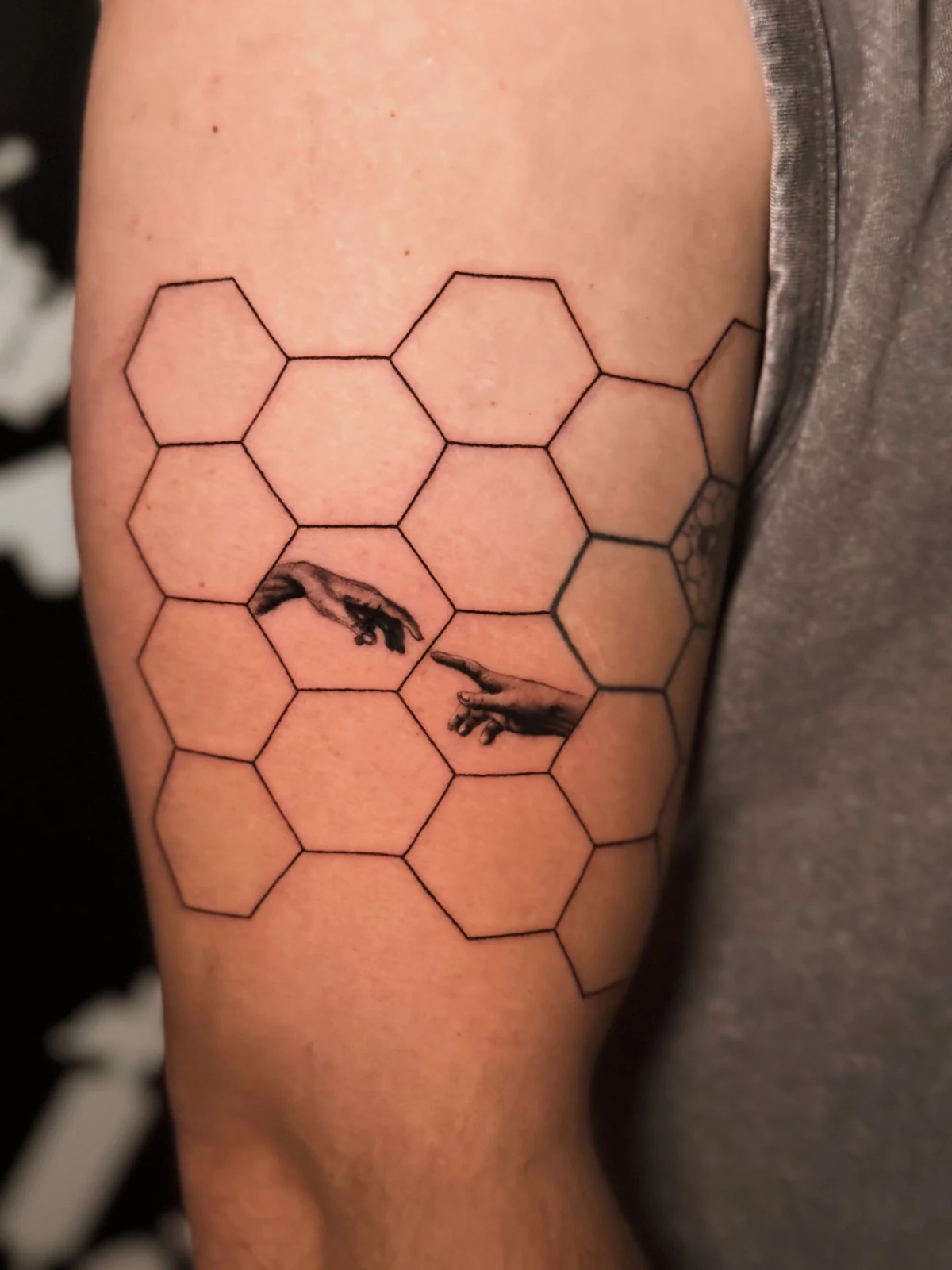 Geometrisches Tattoo mit Wabenmuster und zwei detailreich schattierten Händen am Oberarm – Arbeit von Merci, Skin City Tattoo.